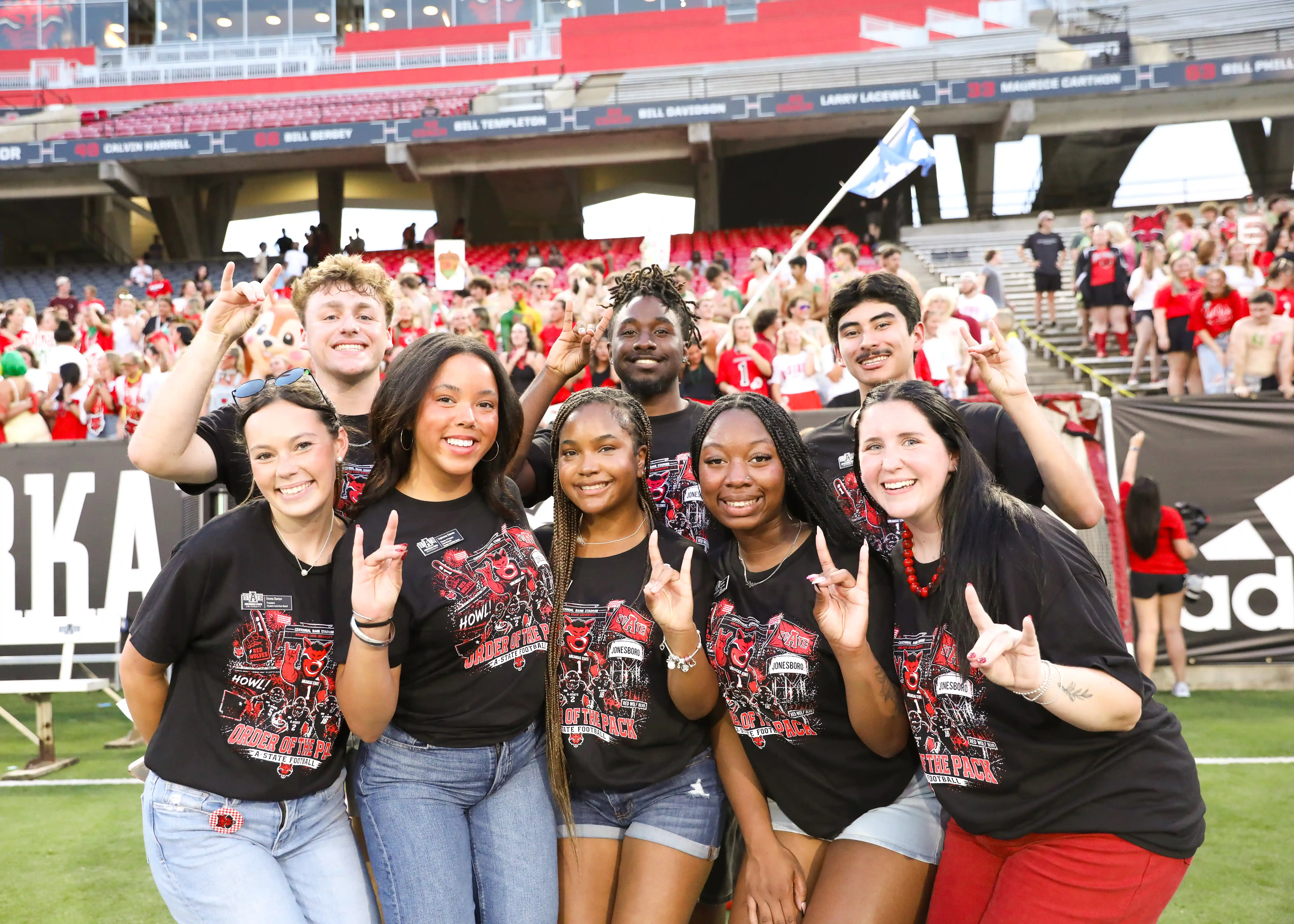 Student Activities Board students with their hands making a 'wolves up' sign in front of a crowd of students at the Order of the Pack pep rally.