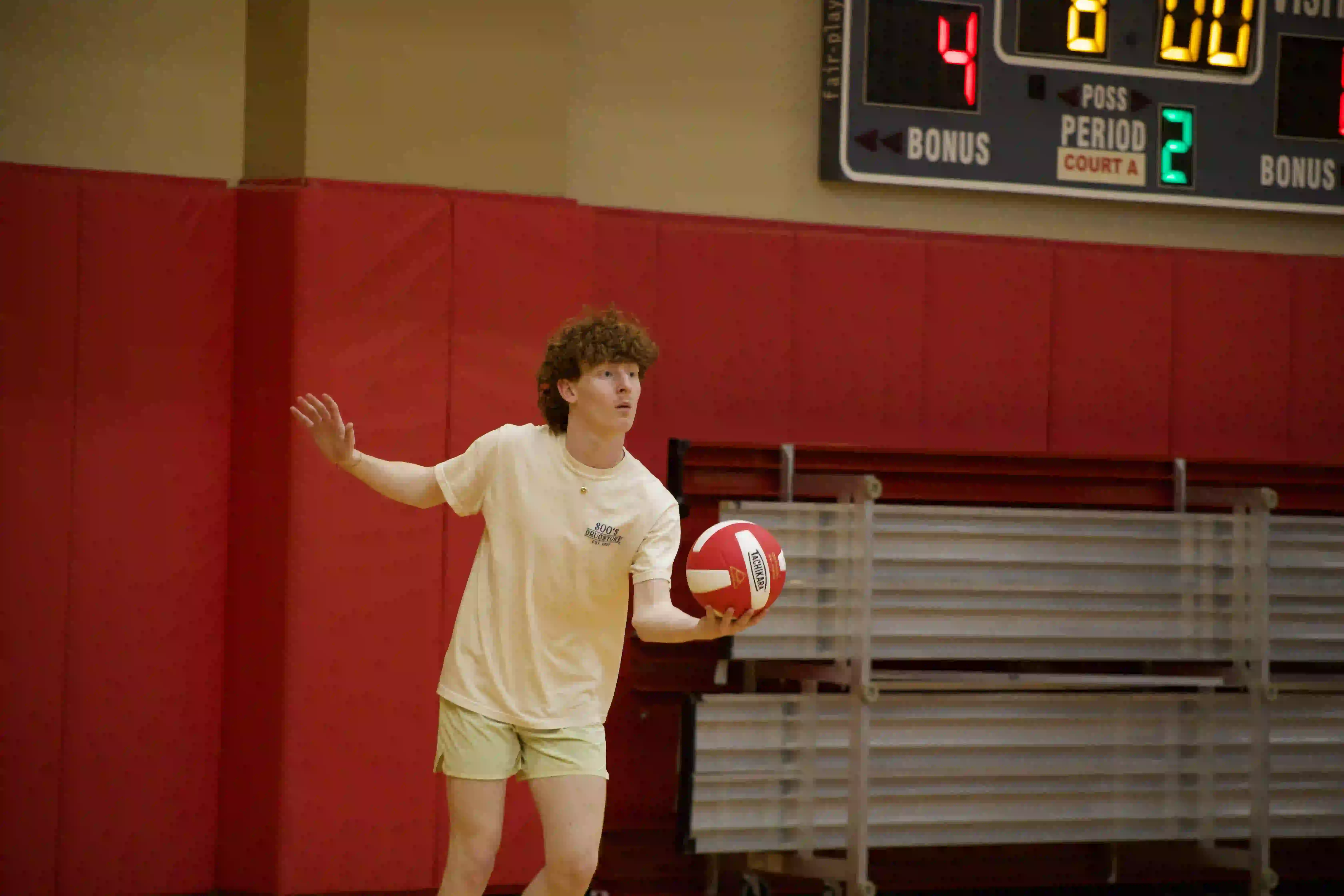Student serving volleyball in gym.