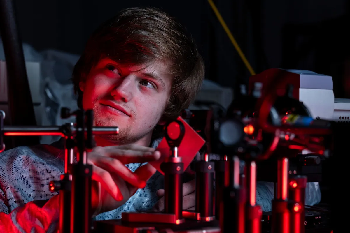 A student sets up a laser experiment in an engineering lab on campus.