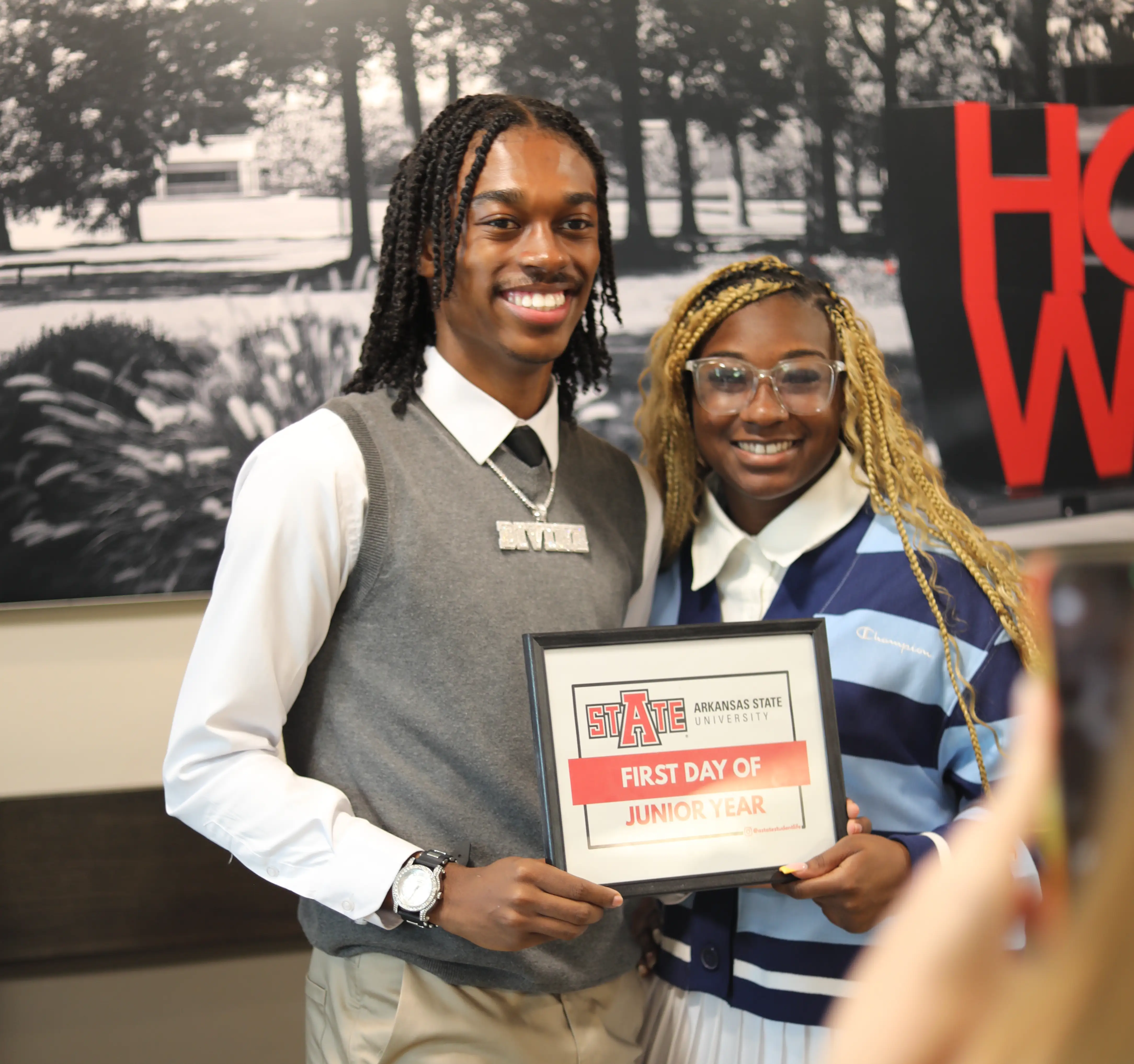 Two students posing in front of backdrop with a sign for the first day of class.