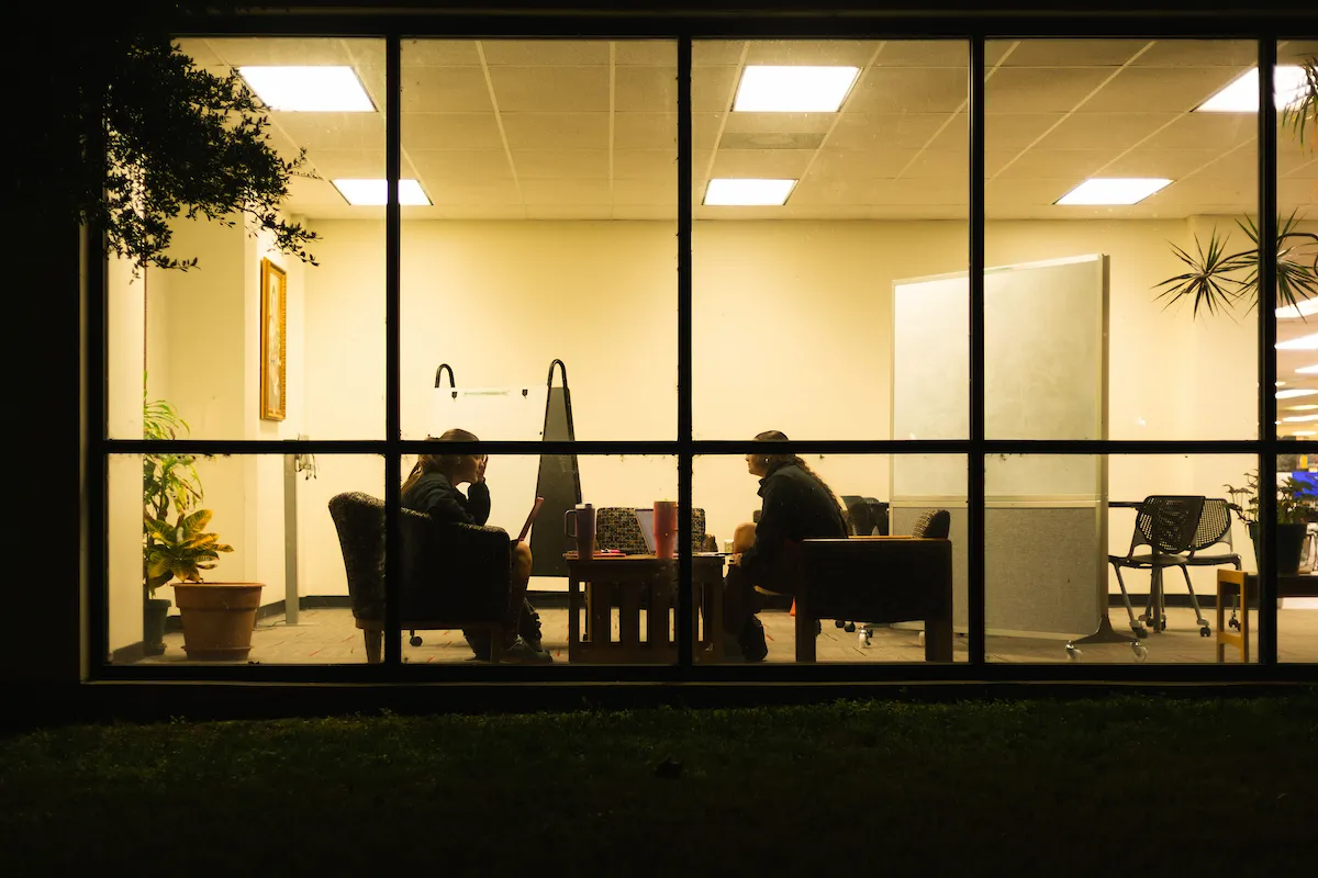 The silhouette of two people meeting through a window during the evening at A-State.
