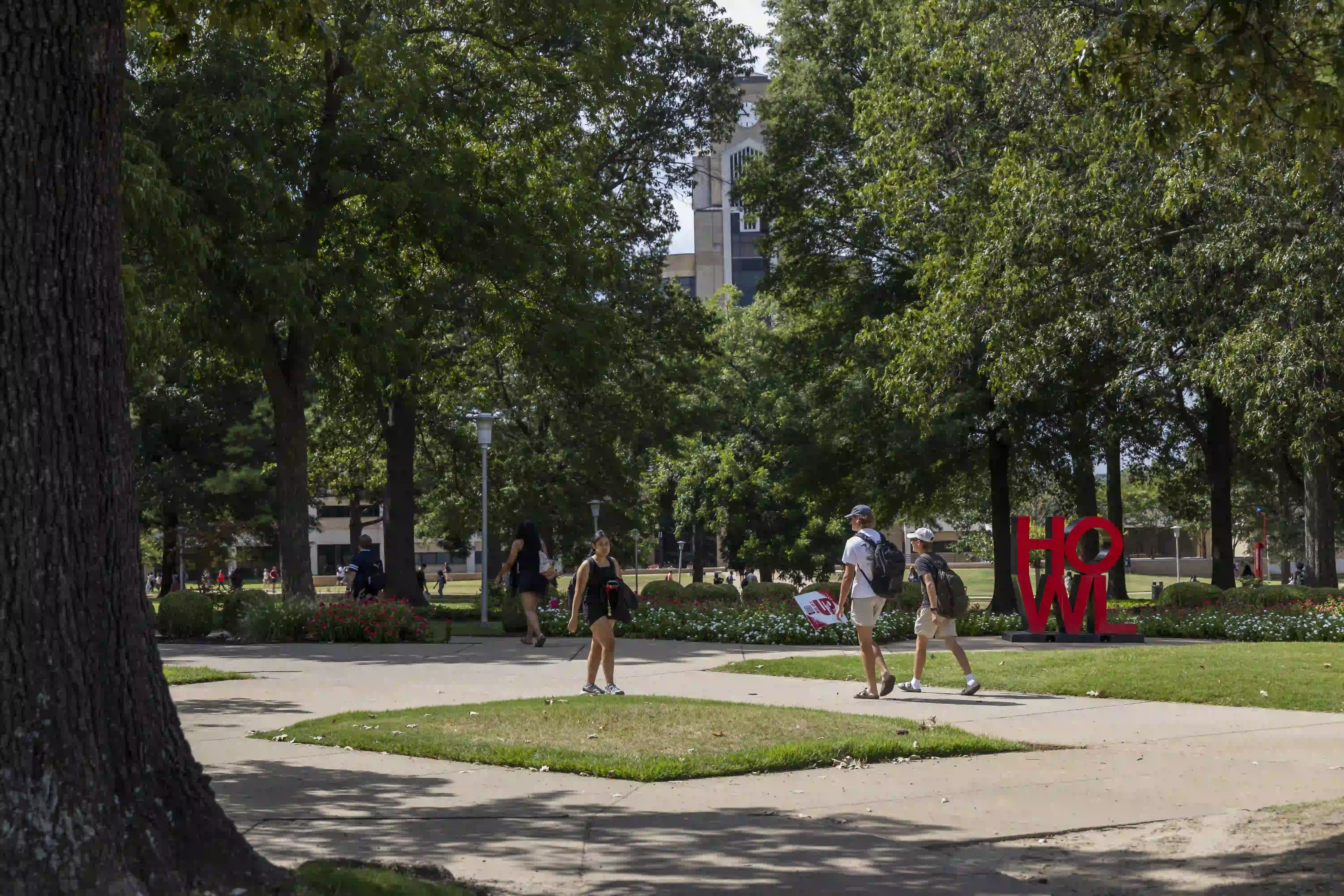 Students walking on sidewalk in front of trees and library building.
