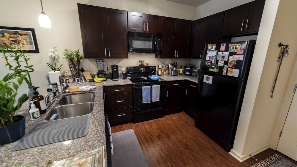 Modern kitchen with dark wood cabinets, granite countertops, black appliances including stove, microwave, and refrigerator, and hardwood flooring.