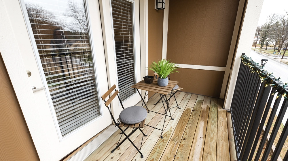 Private balcony with wooden flooring, small table, chairs, and potted plants.