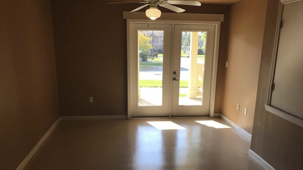 Empty living space with tan walls, ceiling fan, and glass doors opening to a porch.