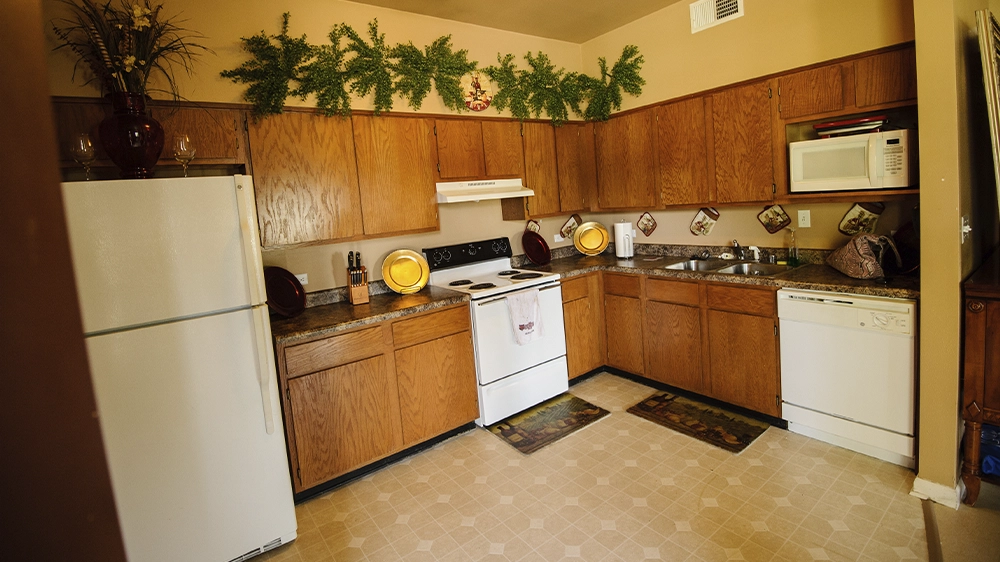 Kitchen with wooden cabinets, white appliances including stove, refrigerator, microwave, and dishwasher, and decorative greenery above cabinets.