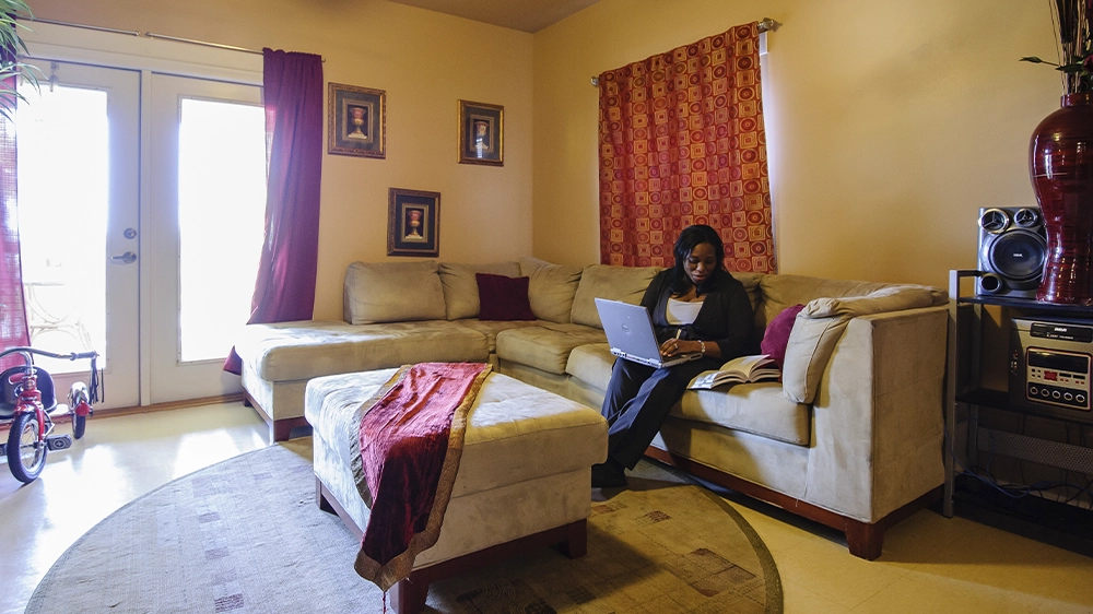 Living room with a beige sectional sofa, ottoman, and entertainment system, featuring glass doors and red curtains.