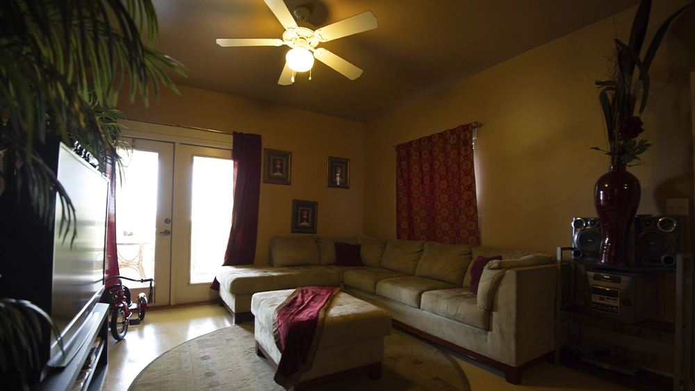 Living room with a beige sectional sofa, ottoman, red curtains, and decorative accents, with glass doors leading to the porch.