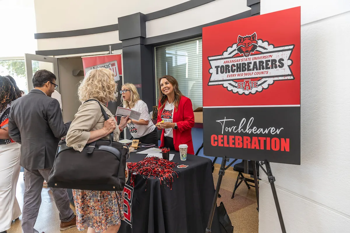 Attendees check in at Torchbearers Celebration table with Arkansas State Red Wolves signage and giveaways.