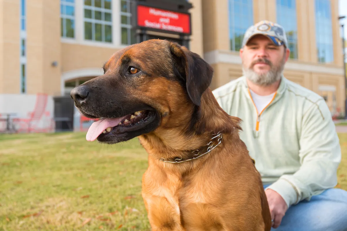 A veteran looks at his support dog in front of the Humanities and Social Sciences Building