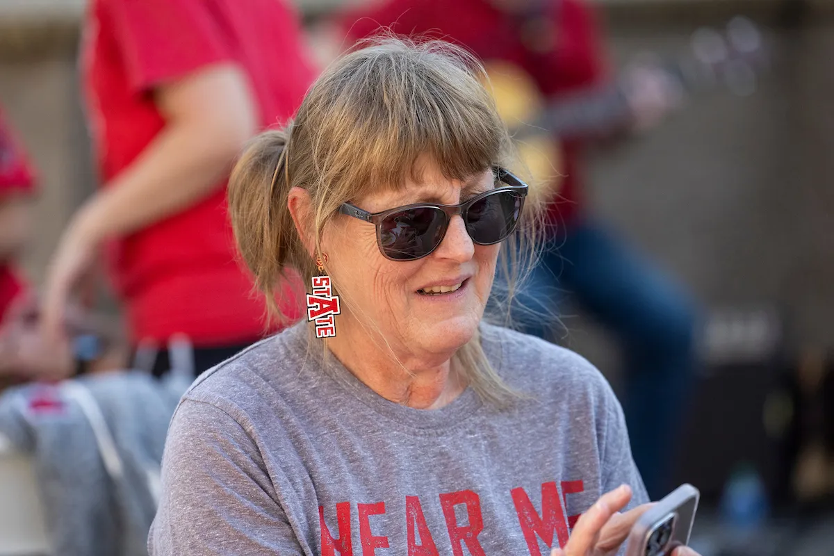 A lady in A-State earrings dials a number on her cell phone.