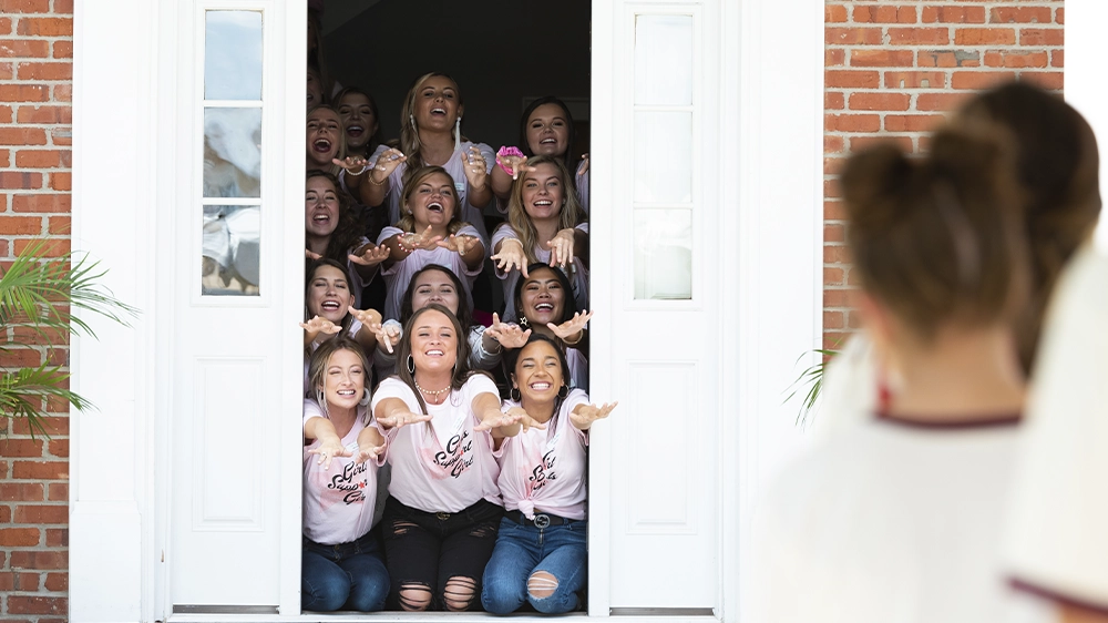 Group standing inside a doorway wearing matching shirts, forming hand signs during recruitment.